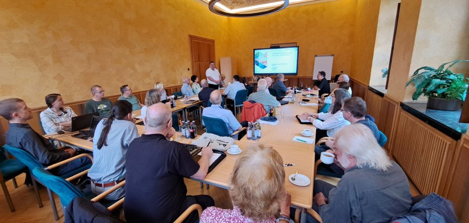 Das Bild zeigt die Teilnehmenden des Workshops über die Ladesäuleninfrastruktur sitzend im Raum. Sie betrachten einen Bildschirm.