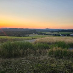 Ein Bild zeigt den Sonnenuntergang über Winnerath. Die letzten Sonnenstrahlen tauchen die Dächer und Felder in goldenes Licht. Der Himmel leuchtet in Orange und Rosa, was dem Ort eine langsam erwachende Atmosphäre verleiht.